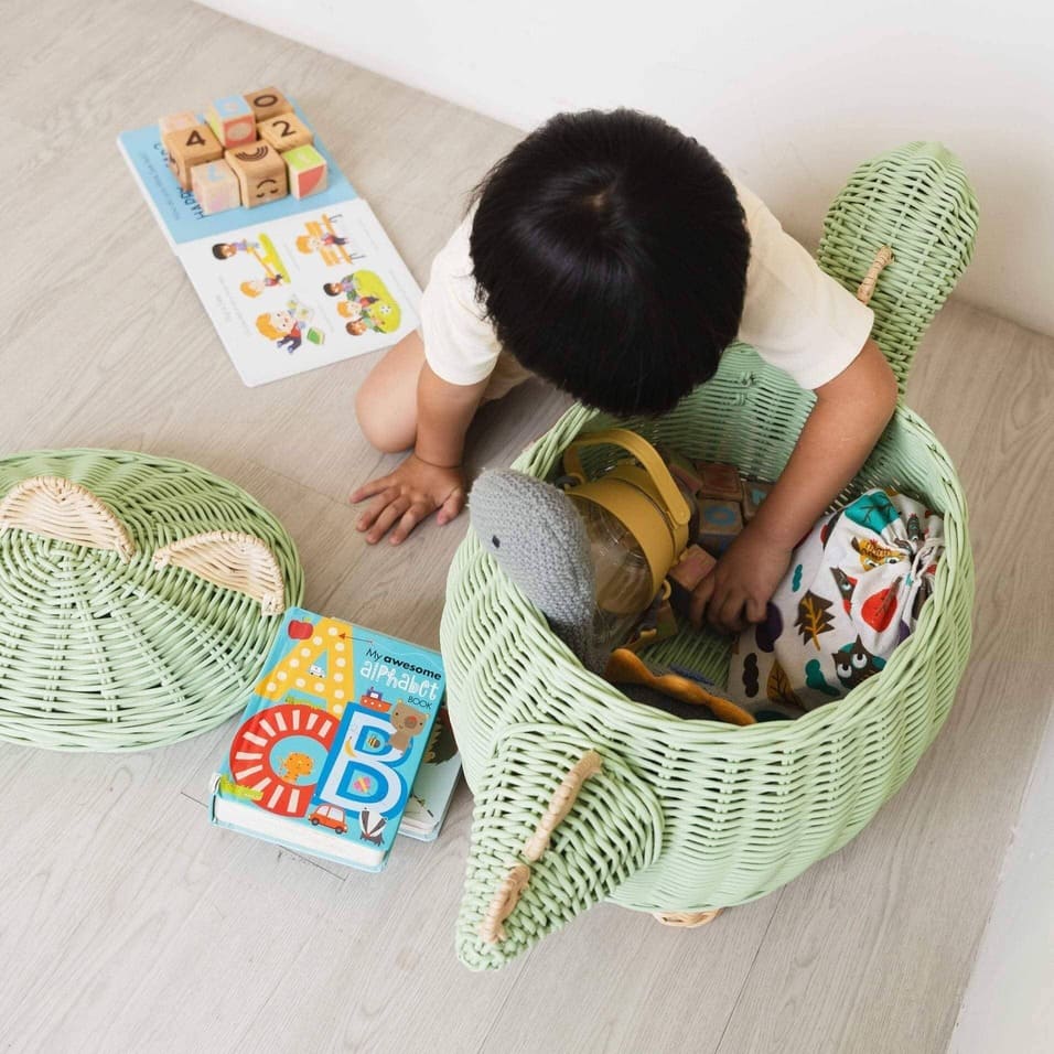 Child cleaning and storing his toys inside the mint green dinosaur rattan storage basket in large size by MOMIJI.