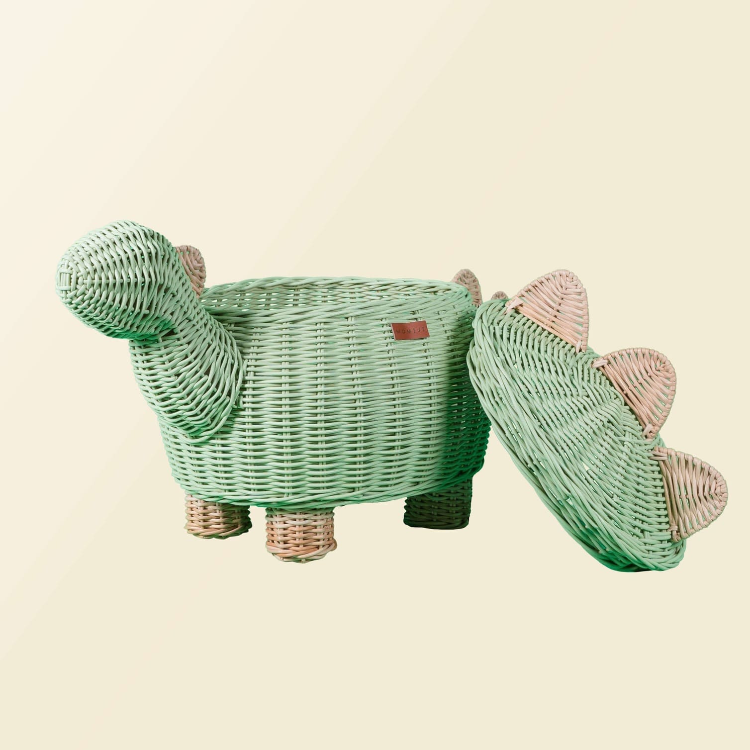Tilted side view of mint green dinosaur rattan storage basket in large size by MOMIJI with lid leaning beside the rattan basket.