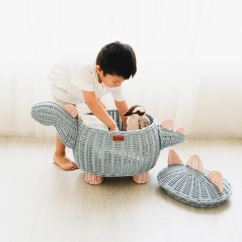 Child picking up a stuffed toy inside pastel blue and pink dinosaur rattan storage basket by MOMIJI.