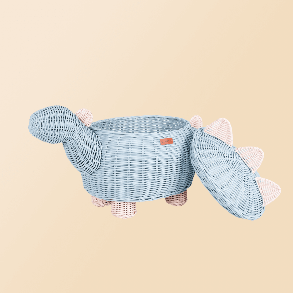 Opened pastel blue and pink dinosaur rattan storage basket by MOMIJI with lid leaning beside the rattan basket.