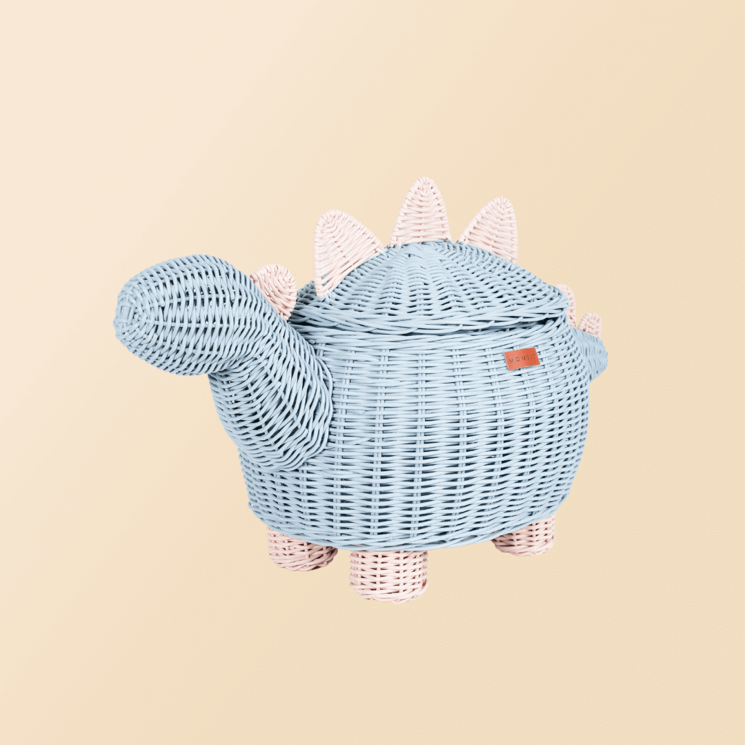 Tilted side view of pastel blue and pink dinosaur rattan storage basket by MOMIJI.
