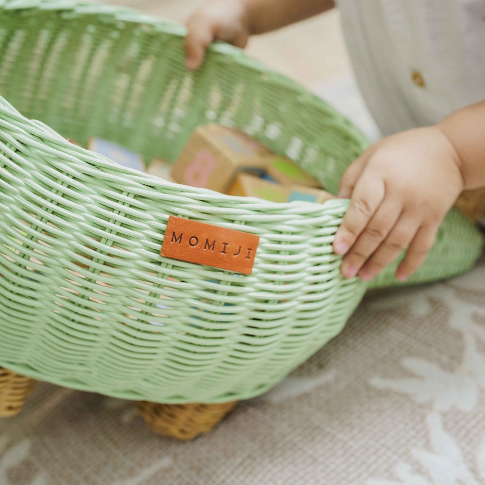 Child holding a handcrafted wicker rattan Dinosaur Storage Basket by MOMIJI, showing the MOMIJI label detail on the side