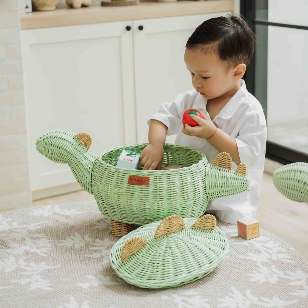 Child placing pretend food toys into a handcrafted wicker rattan Dinosaur Storage Basket by MOMIJI in a kitchen setting