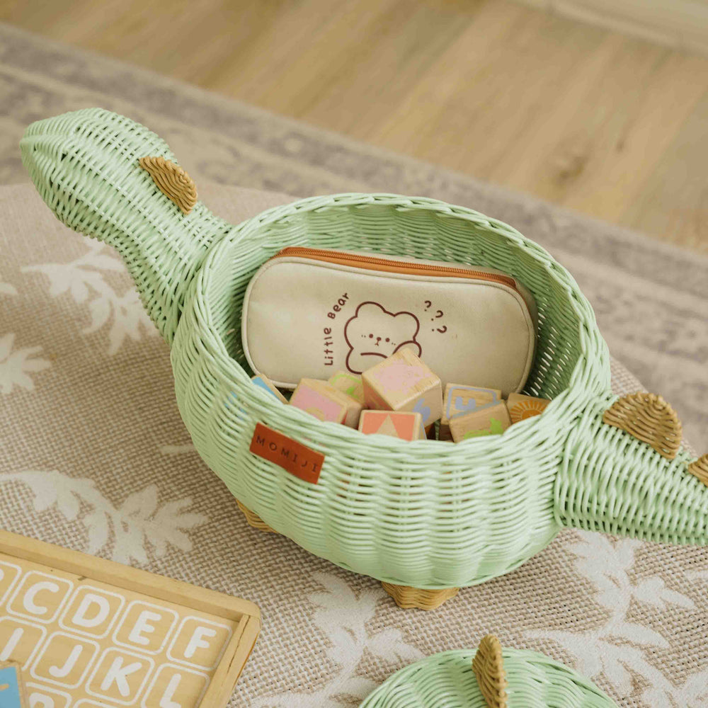 Handcrafted wicker rattan Dinosaur Storage Basket by MOMIJI filled with wooden blocks and a pencil case in a cozy playroom setting