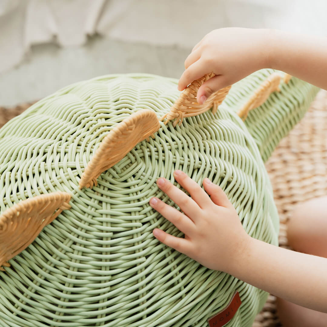 A child holding the spine spikes of the Mint Green Dinosaur Storage Rattan Basket by MOMIJI.