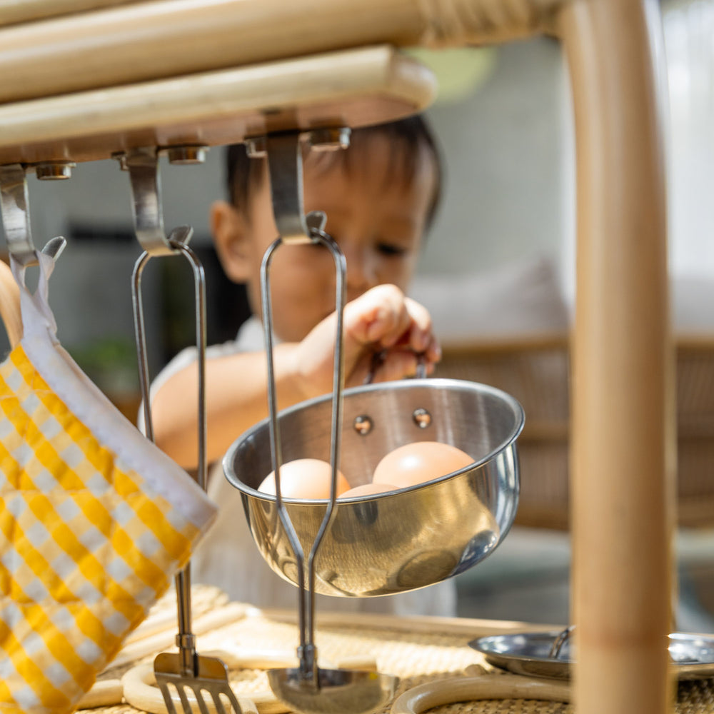 Child interacting with a metal pot containing toy eggs on the Dreamer Play Kitchen by MOMIJI.