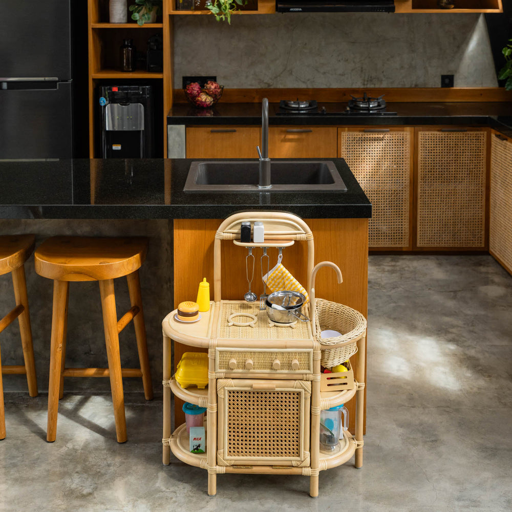 Dreamer Play Kitchen by MOMIJI styled with a rattan cart, stools, and sink in a kitchen area.
