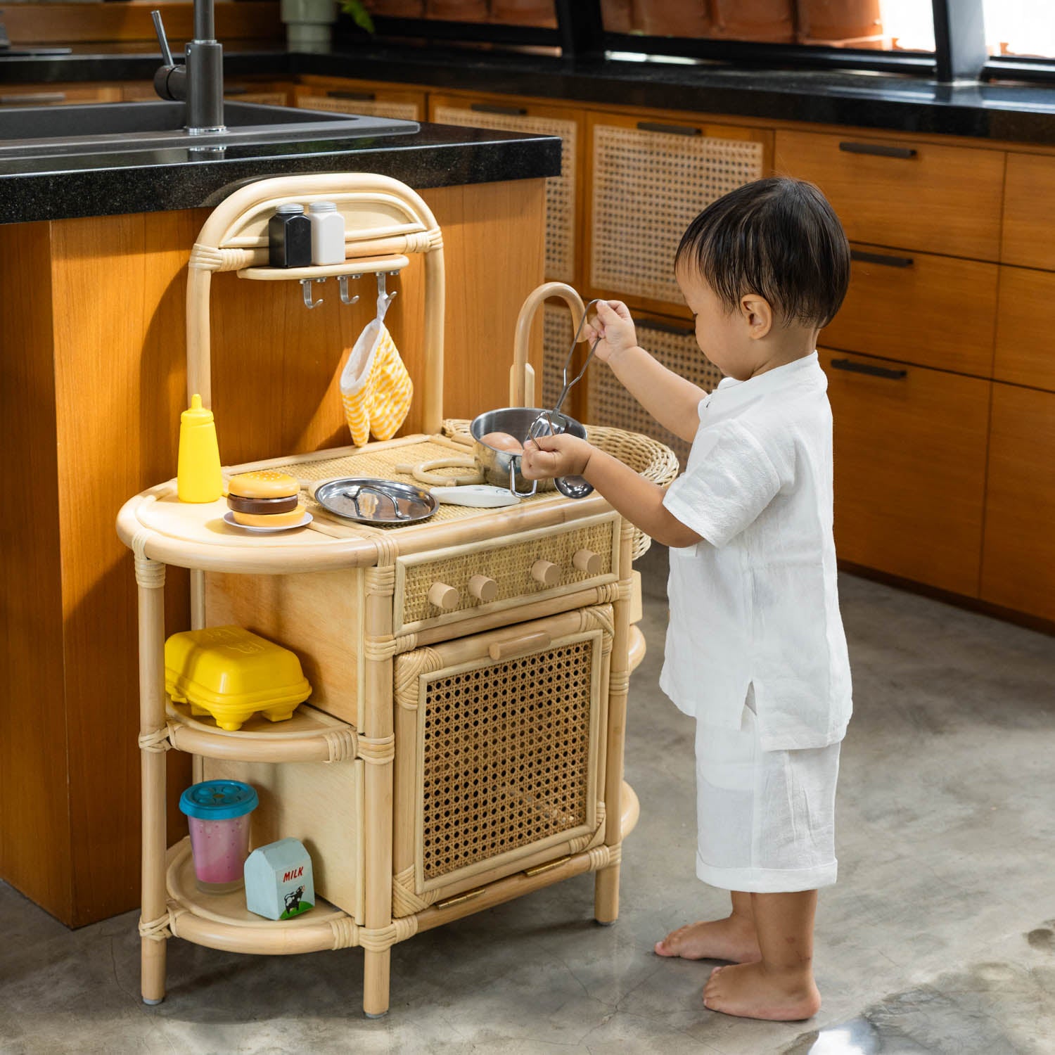 Child playing with the handcrafted rattan wicker Dreamer Play Kitchen by MOMIJI indoors.