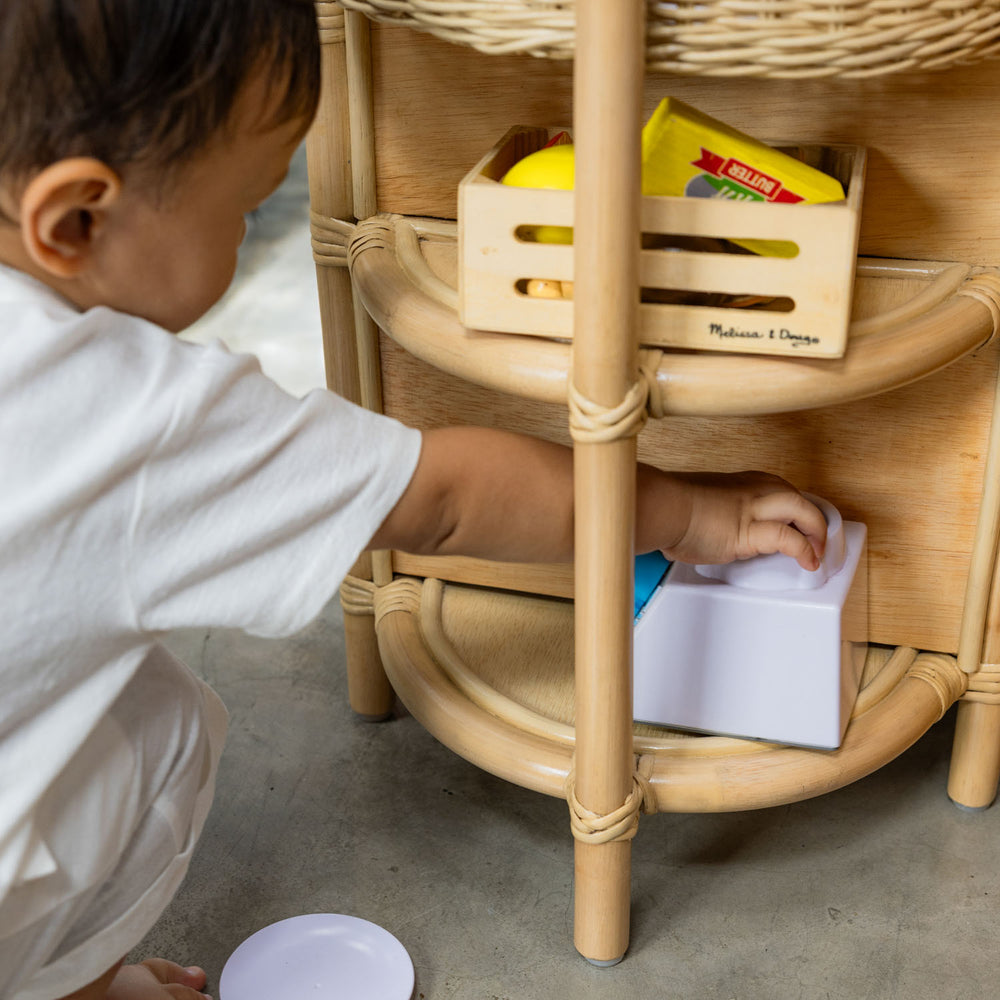 Side view of a child storing toys in the lower storage area of the Dreamer Play Kitchen by MOMIJI.