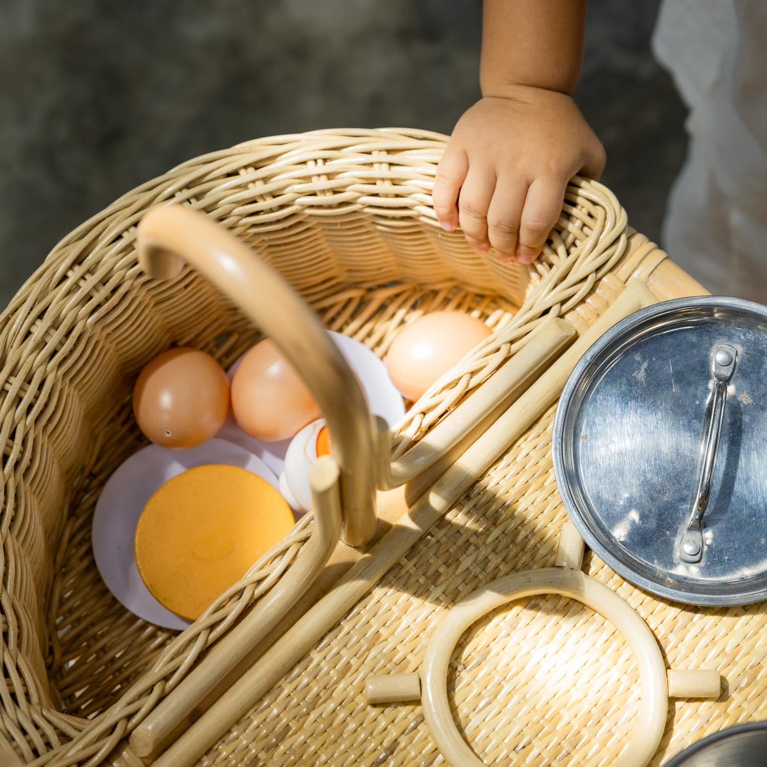 Top view of a child holding the sink area of the handcrafted rattan wicker Dreamer Play Kitchen by MOMIJI.