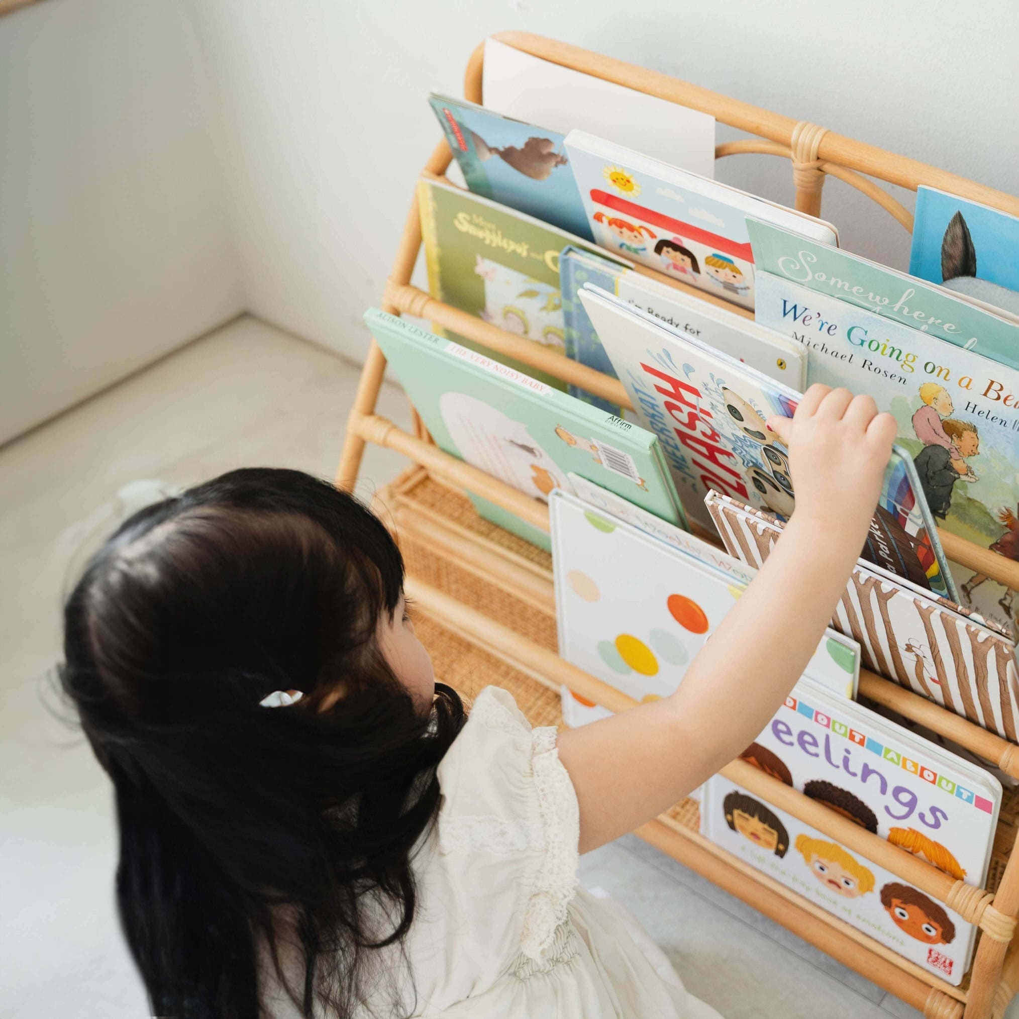 Child reaching for a book in Elena Kids Montessori Bookshelf – Natural by MOMIJI with children's books.