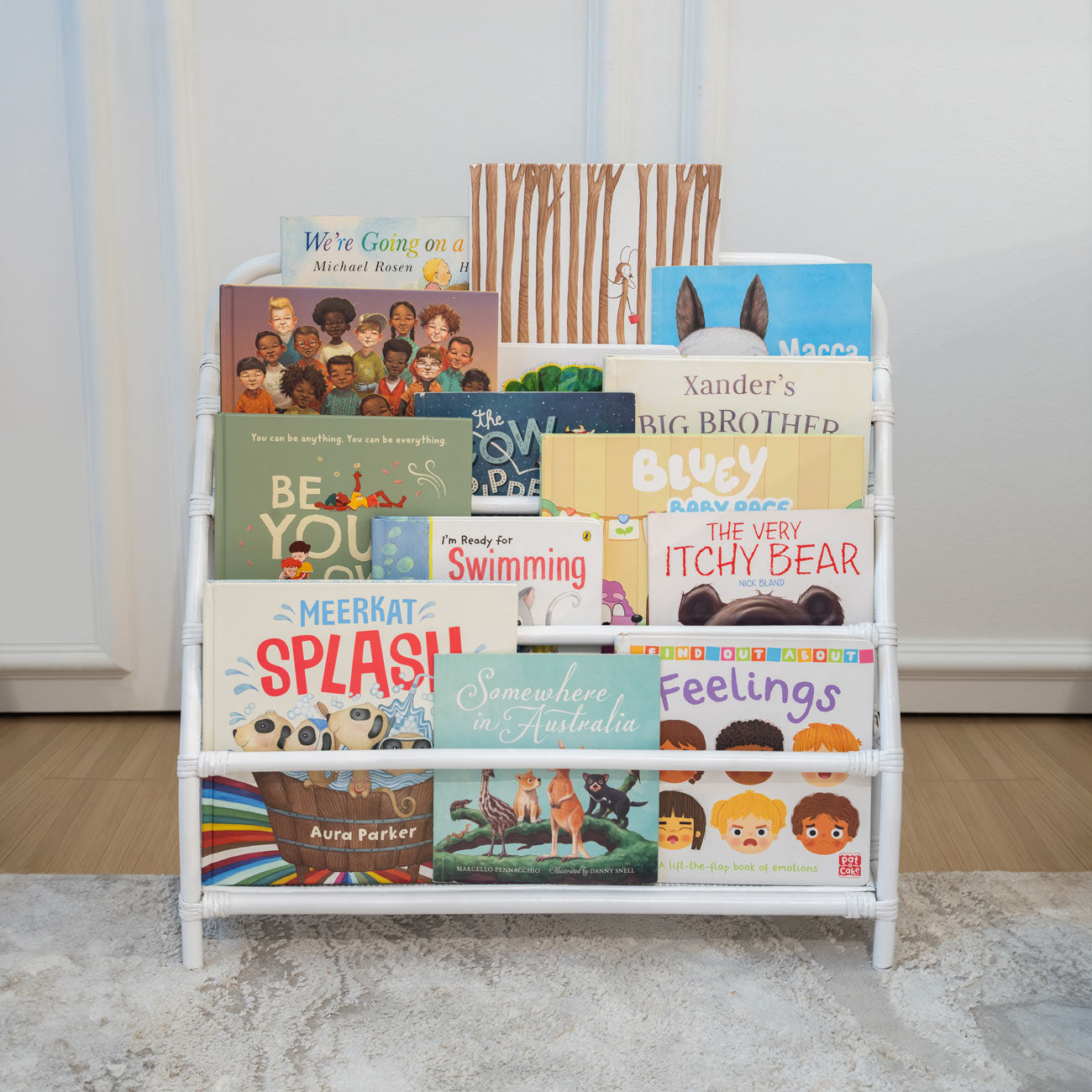 Front view of the handwoven rattan wicker Elena Kids Montessori Bookshelf – White by MOMIJI, styled with children’s books in a living room.