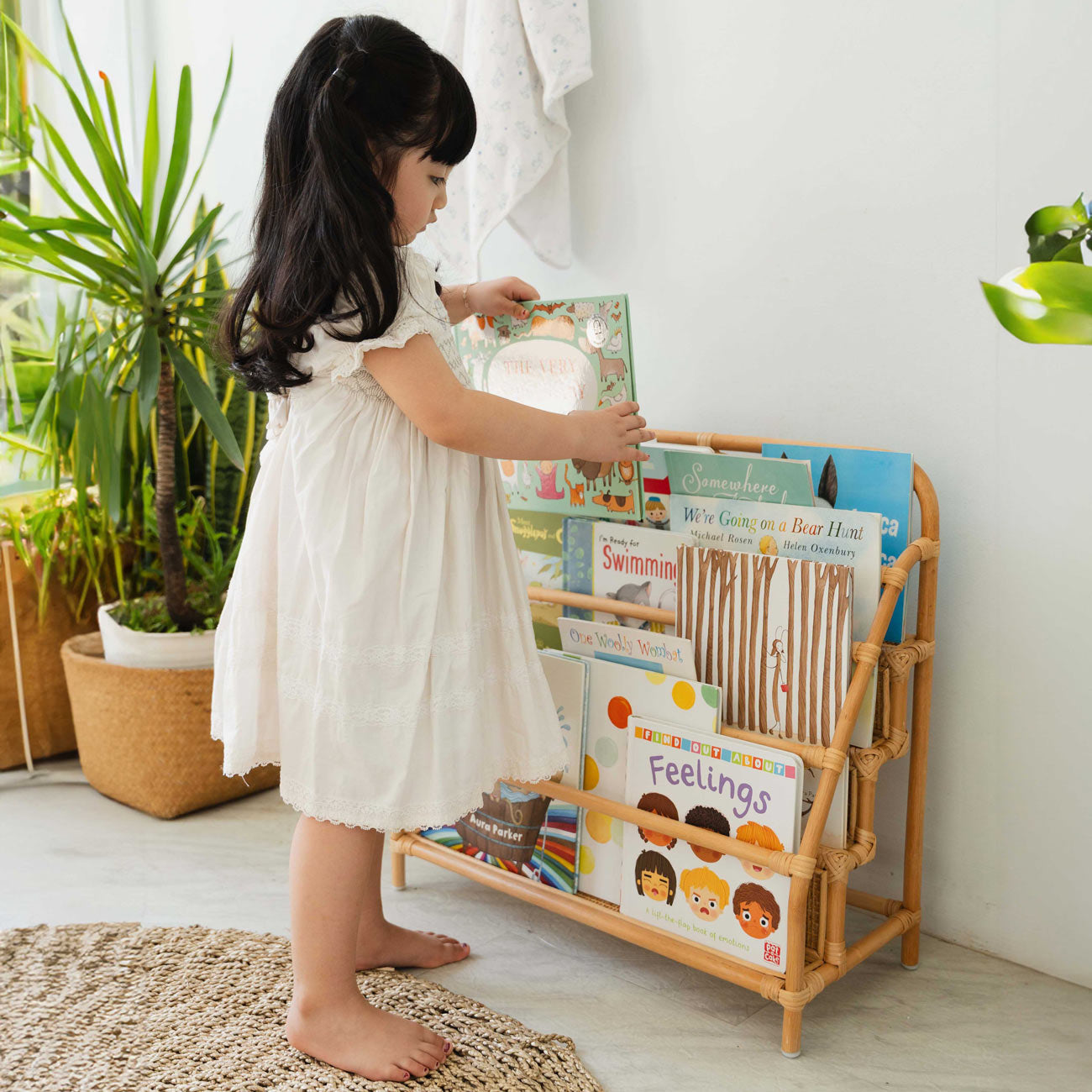 Child storing books to Elena Kids Montessori Bookshelf – Natural by MOMIJI in a room with plants.