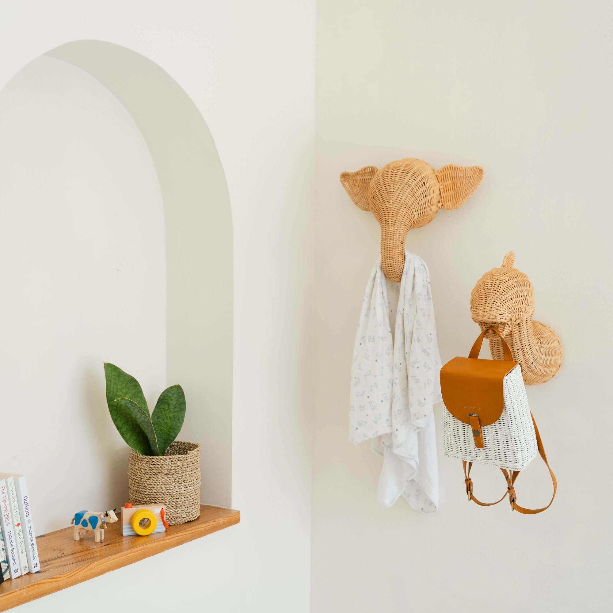 Angled view of the elephant and dinosaur wall decor by MOMIJI hanging clothes and a bag in a decorative room.
