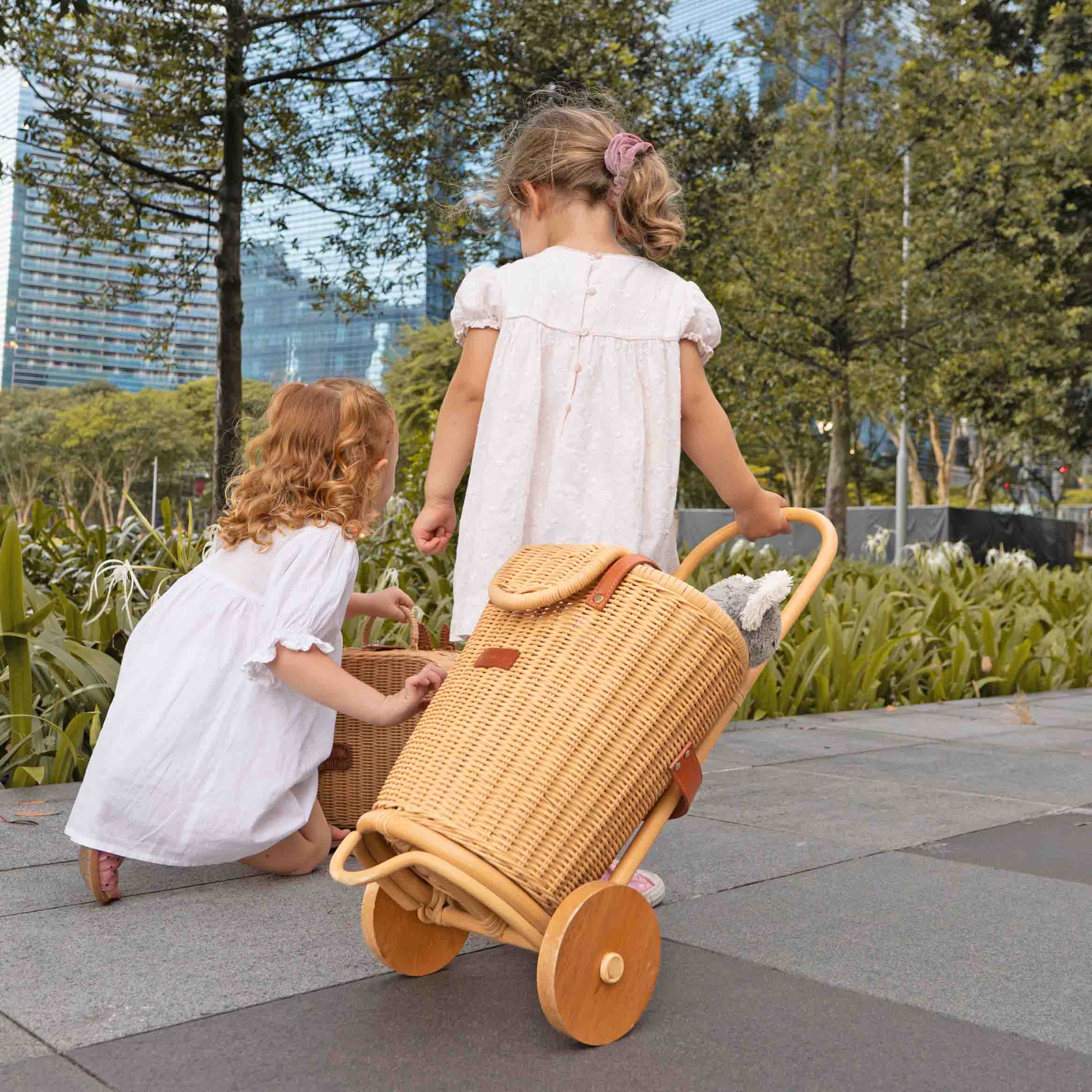 Two children holding the Eric Kids Shopping Trolley by MOMIJI with an extra rattan bag in an outdoor setting.