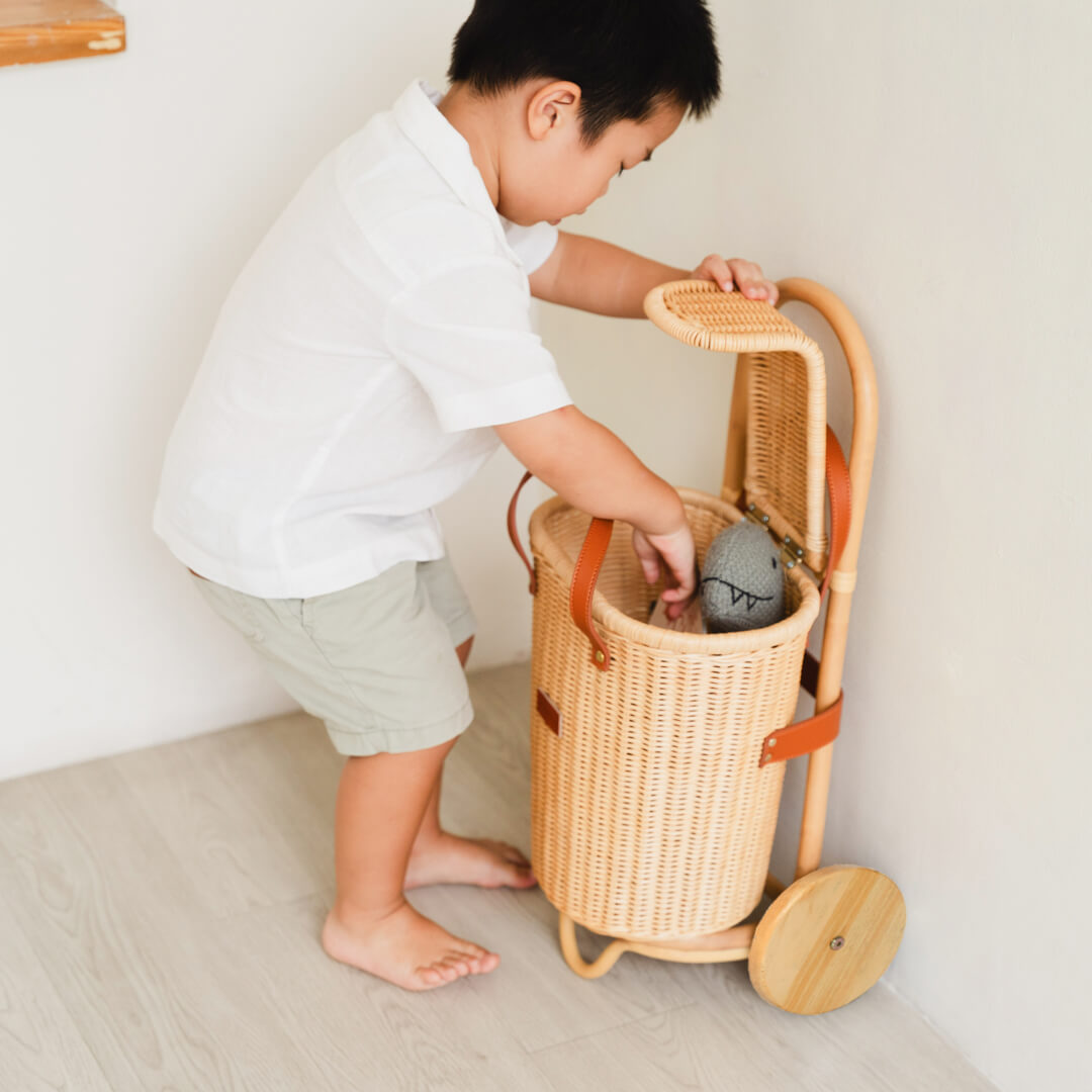 Child placing toys into the Eric Kids Shopping Trolley by MOMIJI in a bright room.