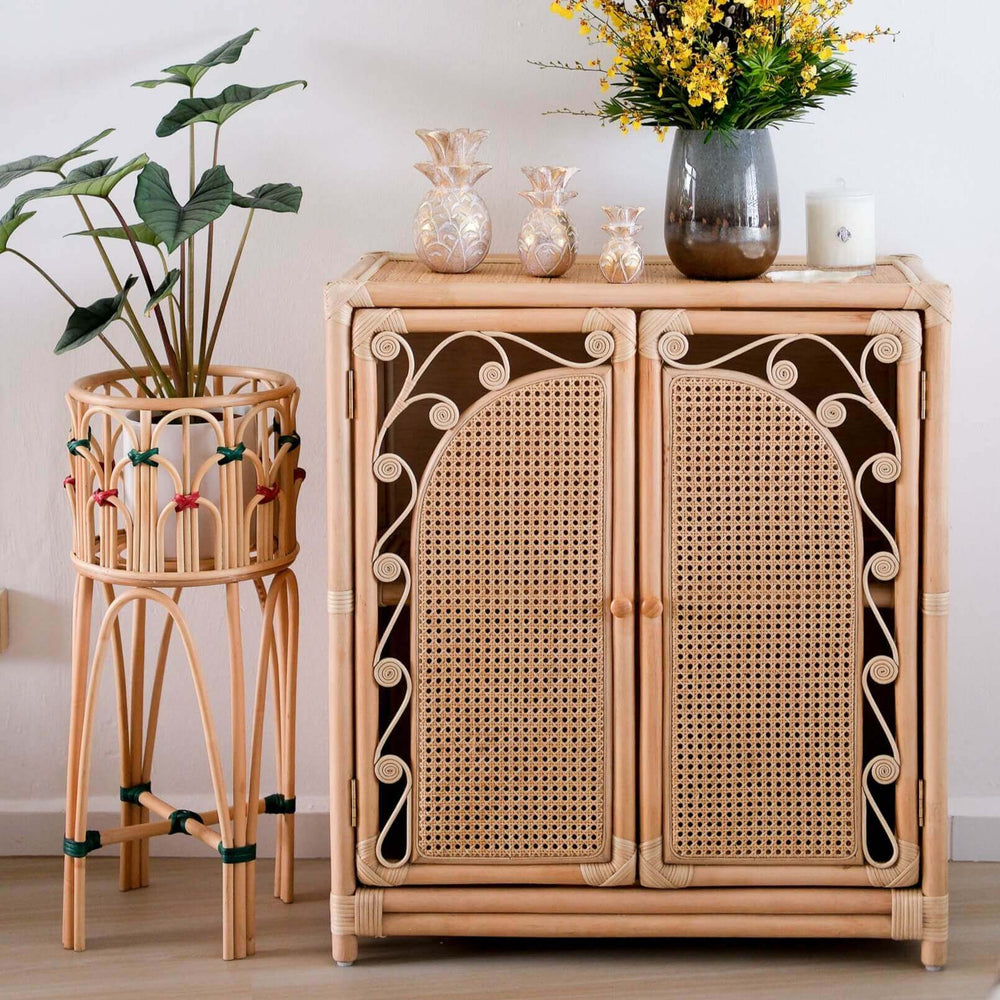 Handcrafted rattan Fern Storage Cabinet by MOMIJI styled with decorative objects and a rattan plant stand in a room setting.