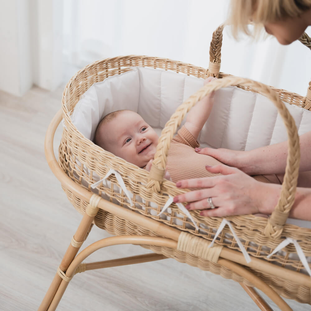 Smiling baby lying in a wicker Moses basket on a fixed stand by MOMIJI.