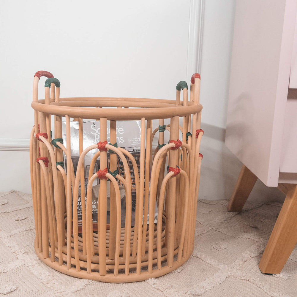 Stacked Floret handcrafted rattan wicker baskets by MOMIJI filled with books beside a cabinet on a rug.