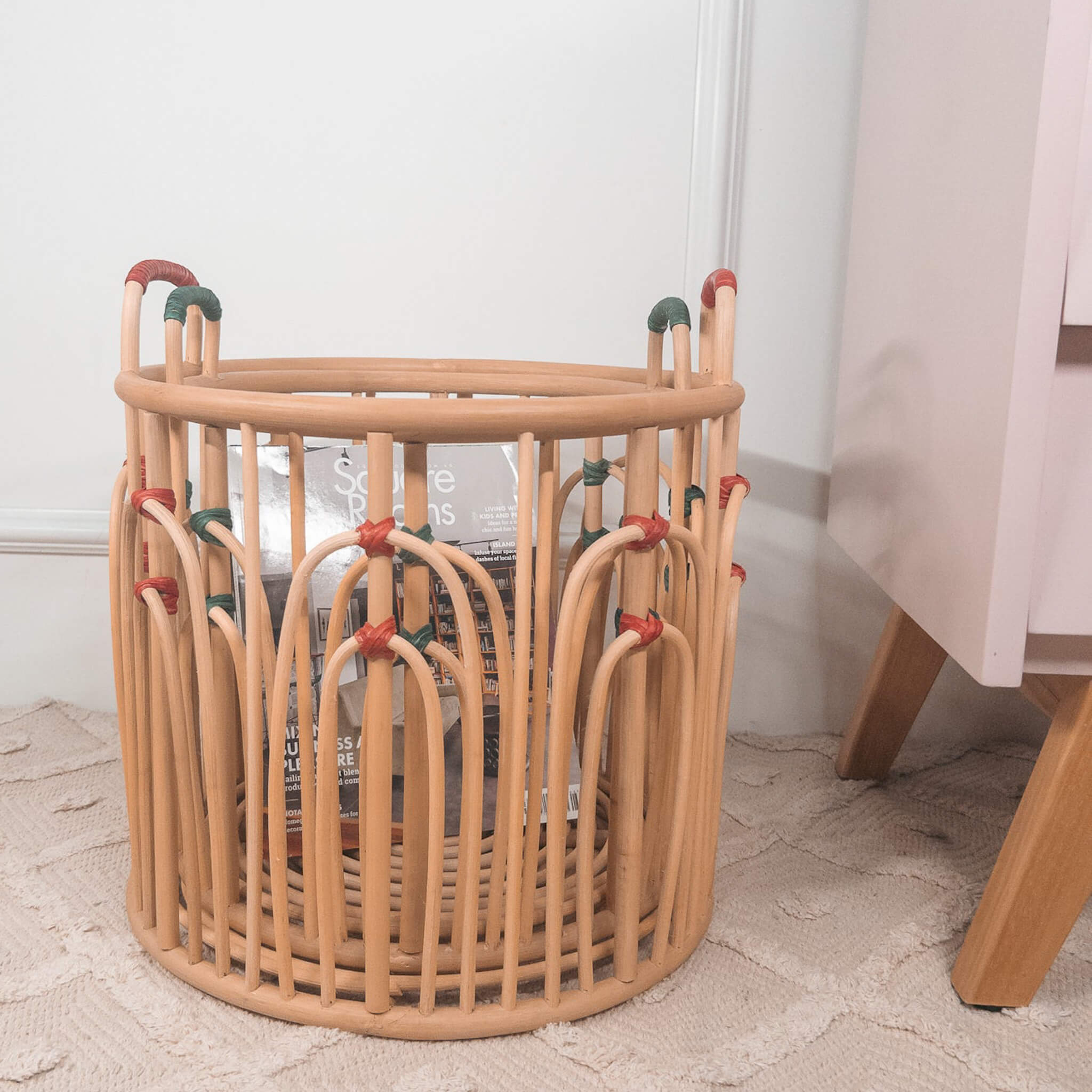 Stacked Floret handcrafted rattan wicker baskets by MOMIJI filled with books beside a cabinet on a rug.
