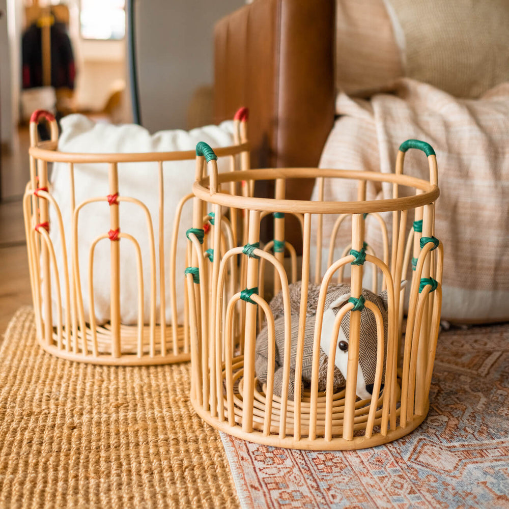 Large and small handcrafted rattan wicker Floret baskets by MOMIJI placed on a rug with a sofa in the background.