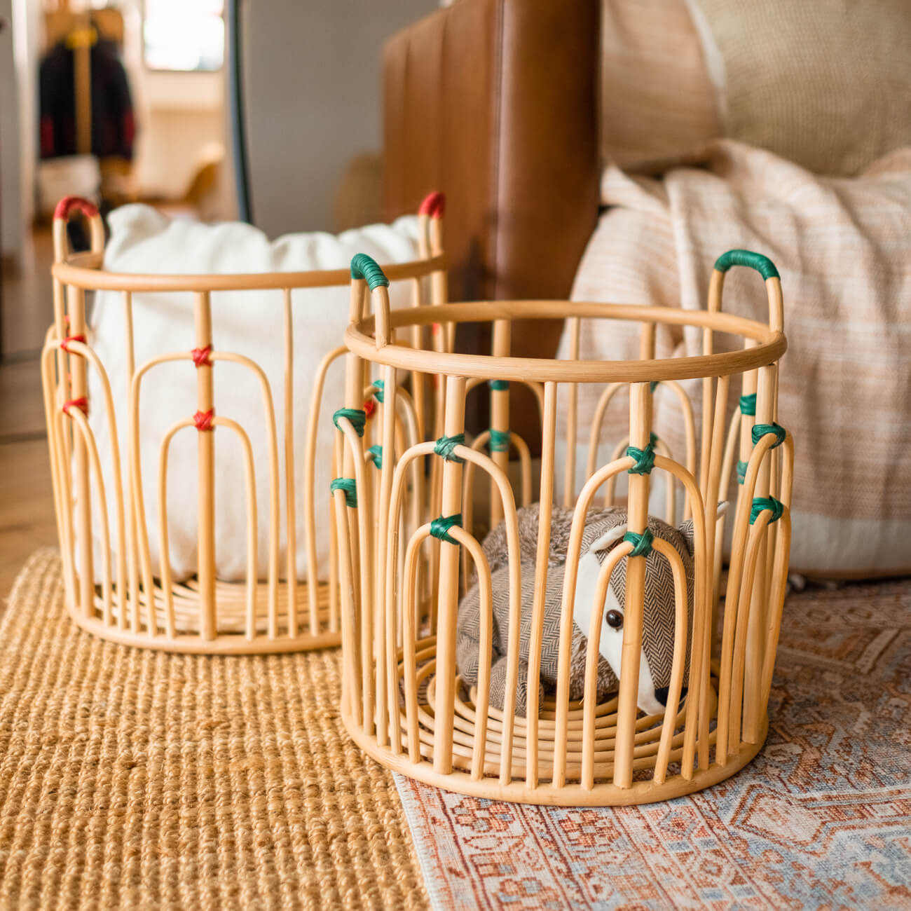 Large and small handcrafted rattan wicker Floret baskets by MOMIJI placed on a rug with a sofa in the background.