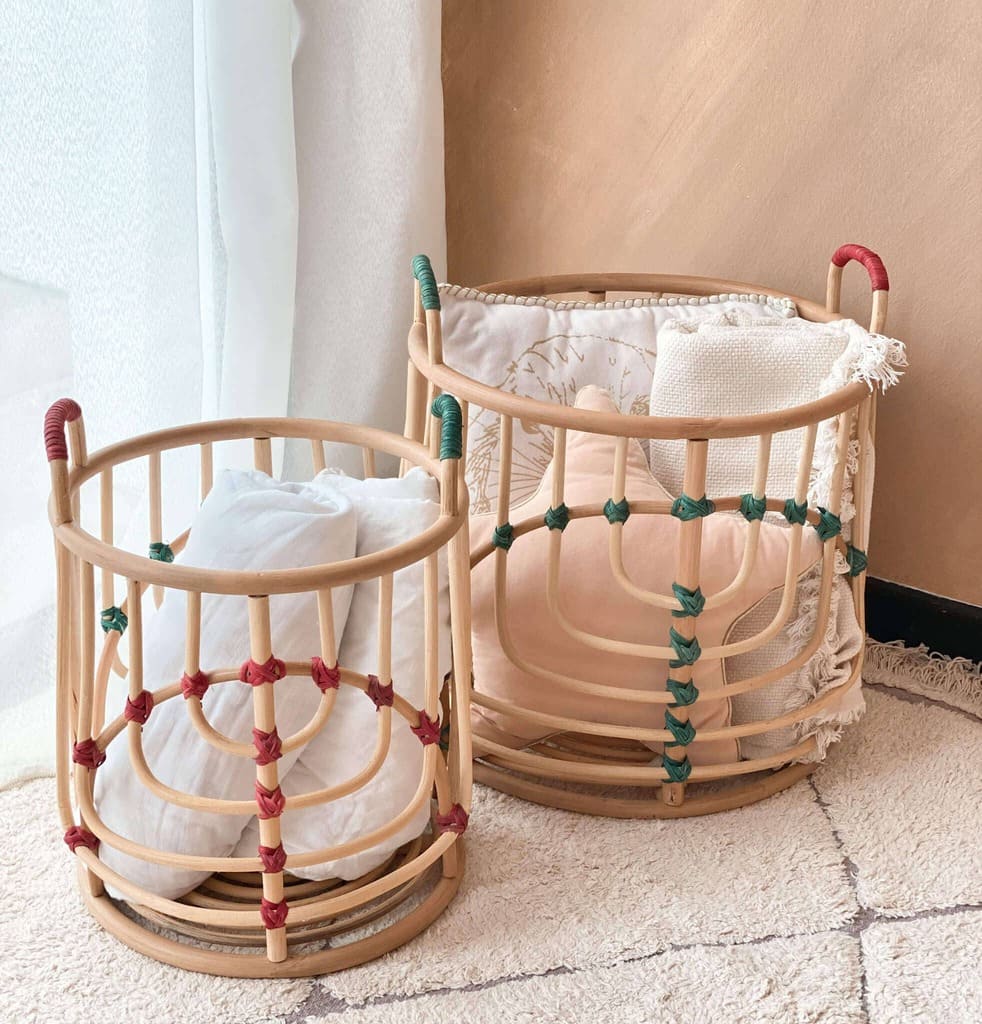 Front view of the handcrafted Iris baskets set by MOMIJI in natural rattan with green and red bindings, filled with cushions, placed on a rug in an indoor setting.