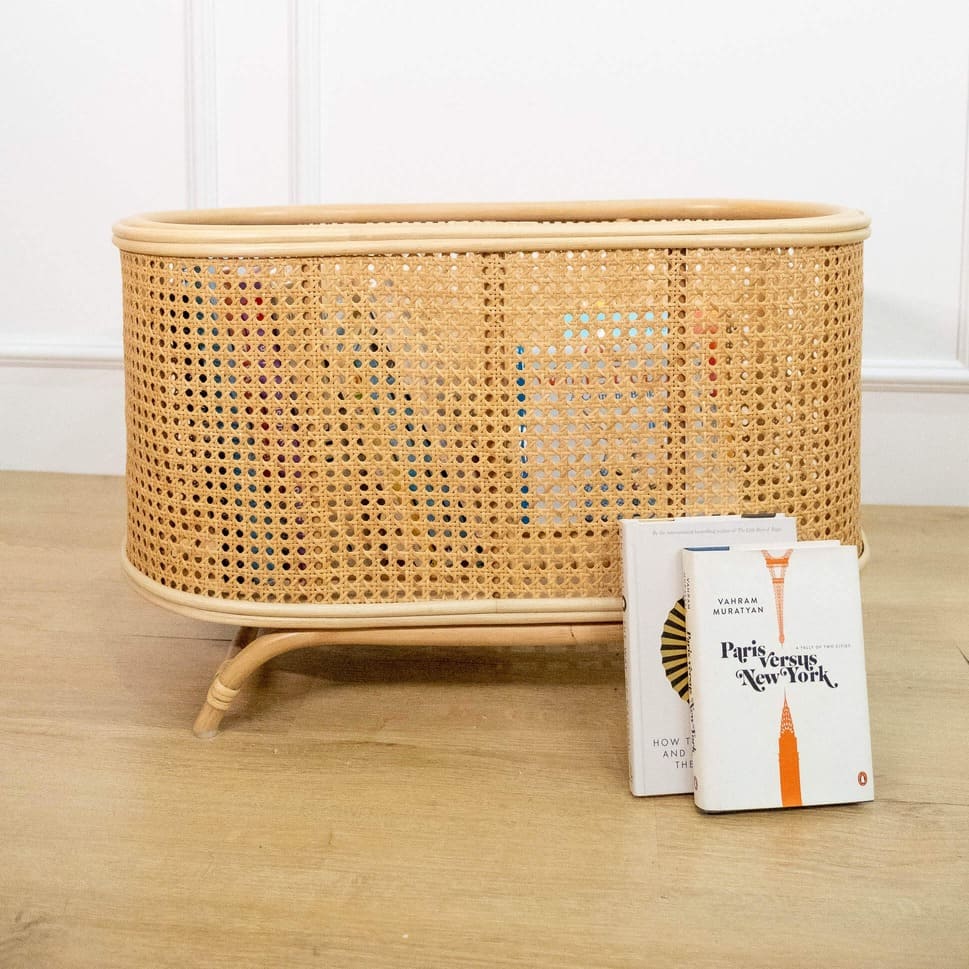 Books placed on the floor with the Isle Wicker Plant Stand by MOMIJI in an indoor setting.