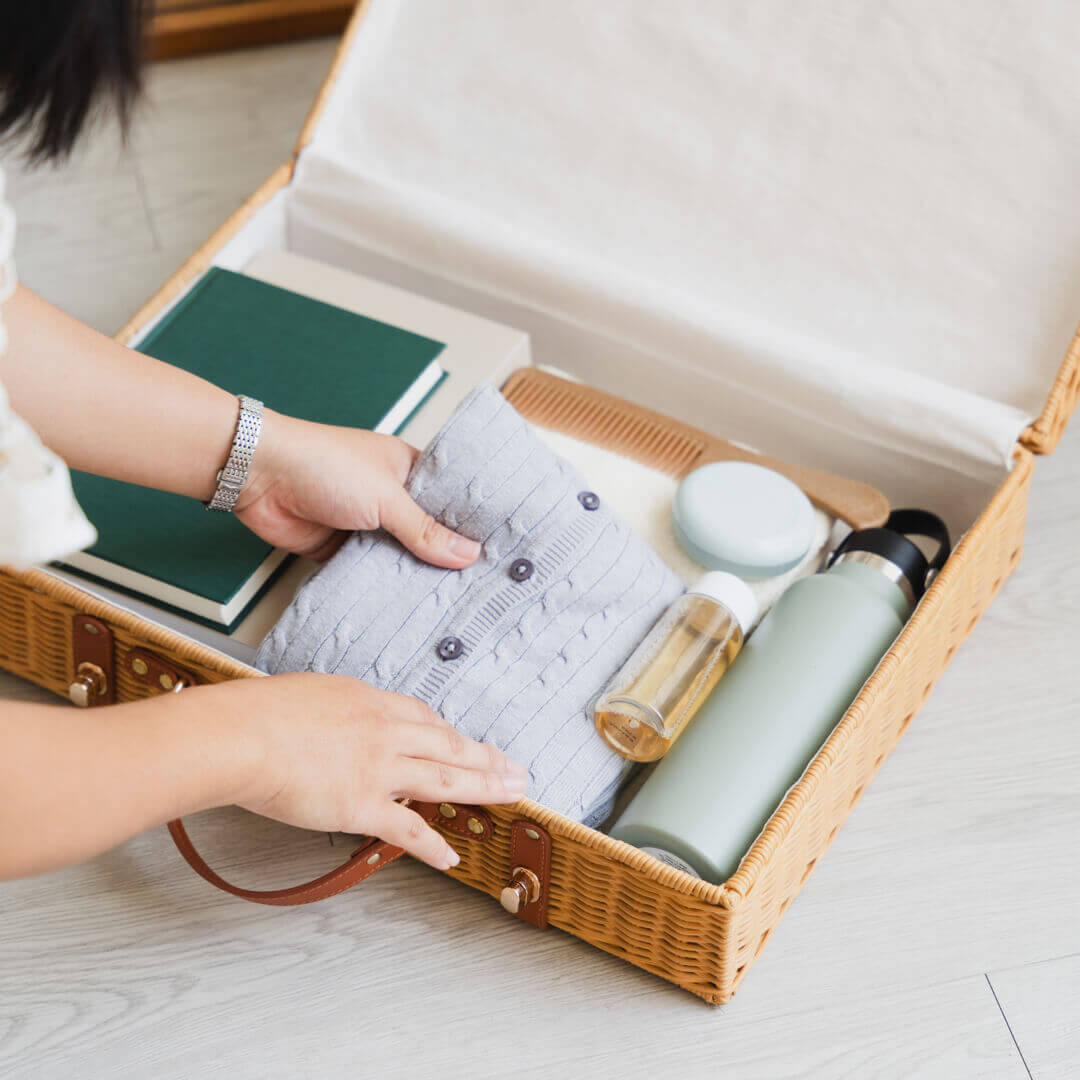Woman placing clothes into the Jasmine rattan Suitcase by MOMIJI while packing indoors.