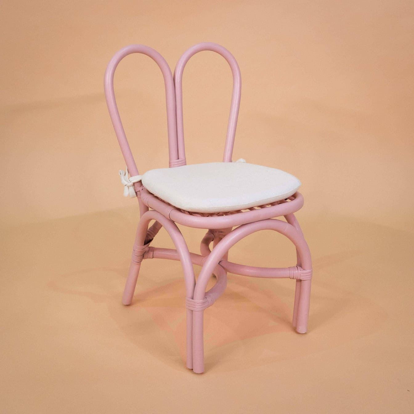 Angled view of the Kids Bunny Chair by MOMIJI in pink with a white cushion.