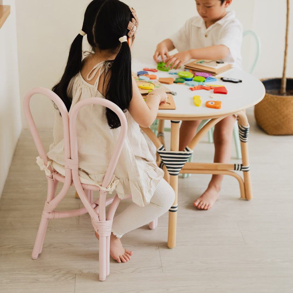 Two children sitting on pink and mint Kids Bunny Chairs by MOMIJI playing with colorful toys at a round table.