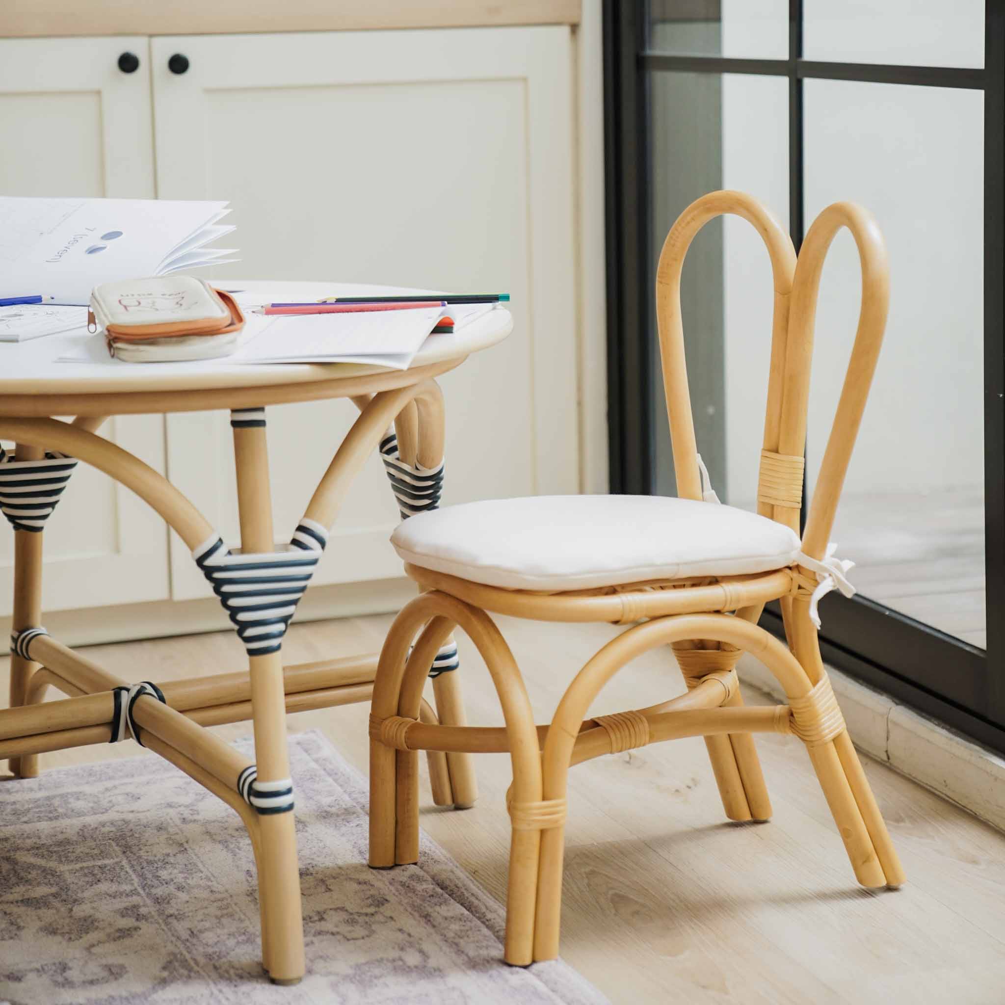 Handcrafted rattan Kids Bunny Chair by MOMIJI in natural with a white cushion, styled in a brightkids room with a rattan table.