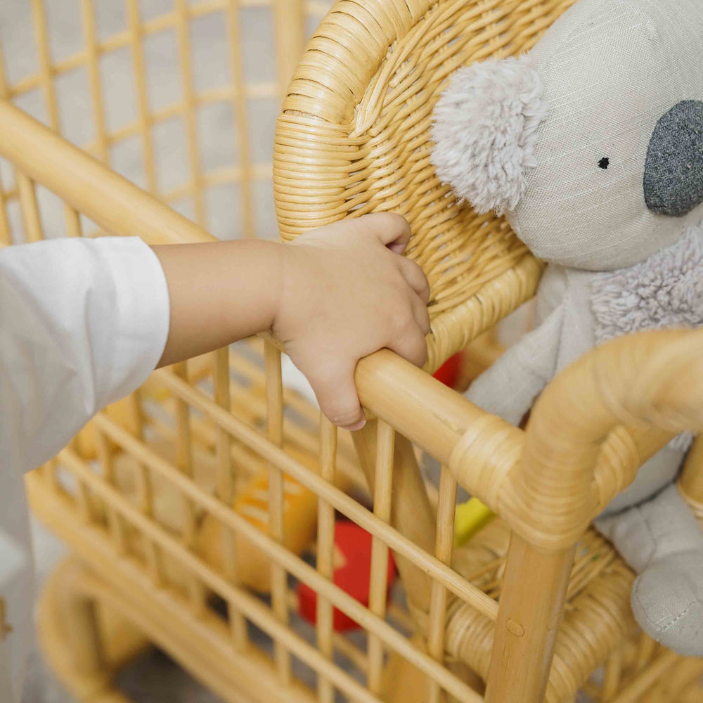 Child holding the side frame of a handcrafted wicker rattan Kids Shopping Cart by MOMIJI, highlighting its sturdy and child safe design