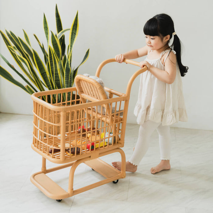 Girl pushing the handcrafted rattan Kids Shopping Cart by MOMIJI filled with toys in an indoor playroom.