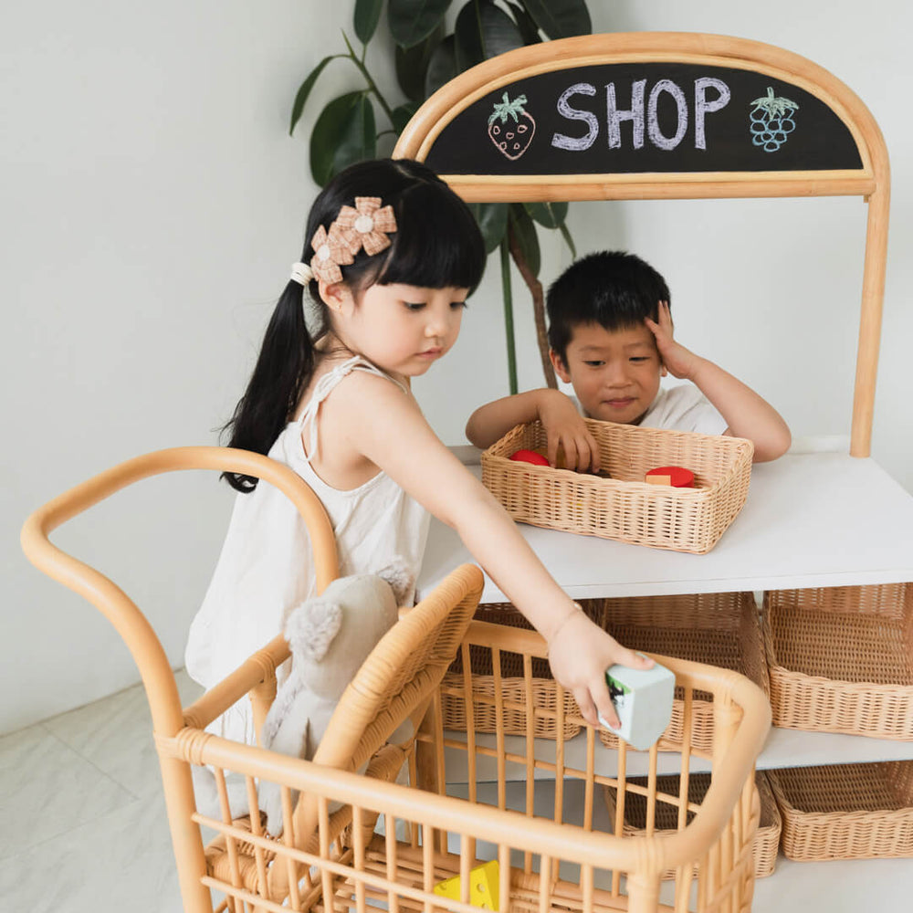 Two children playing and placing items into the Kids Shopping Cart by MOMIJI.