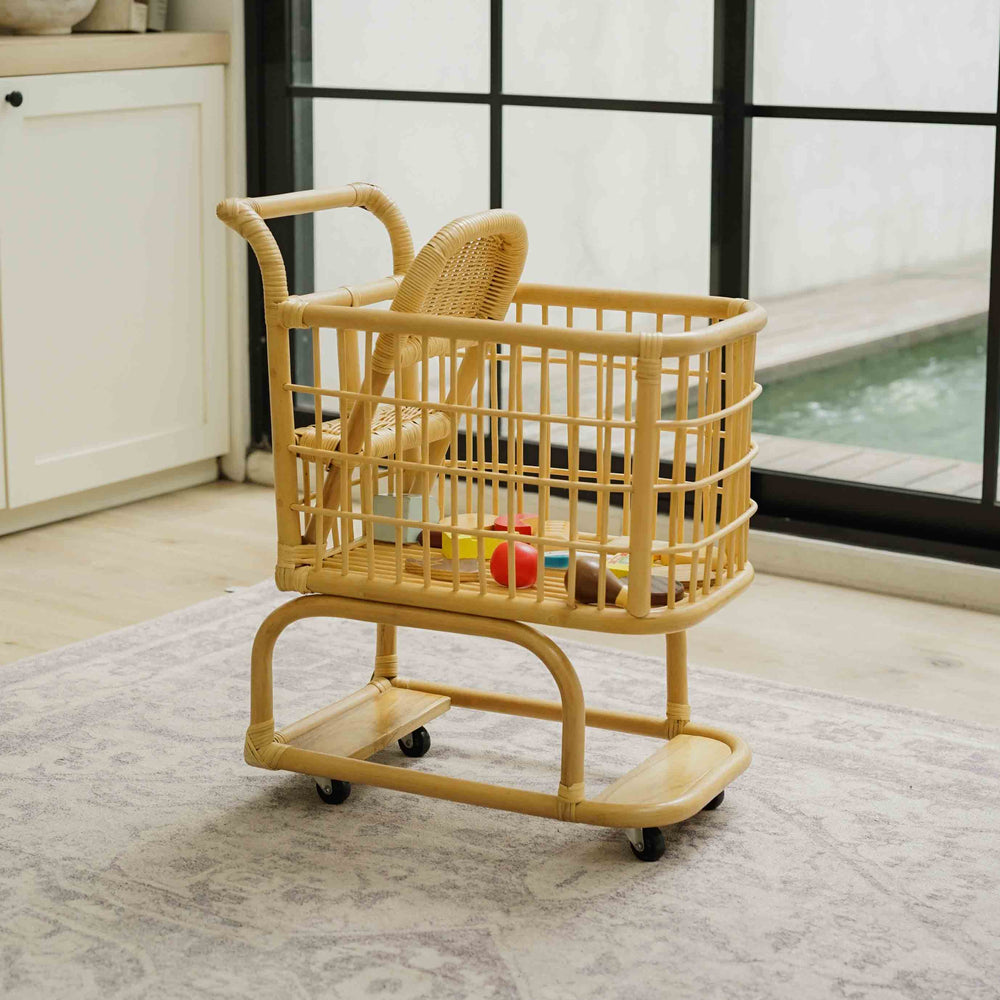 Side view of a handcrafted wicker rattan Kids Shopping Cart by MOMIJI featuring smooth rolling wheels and a spacious basket filled with grocery toys
