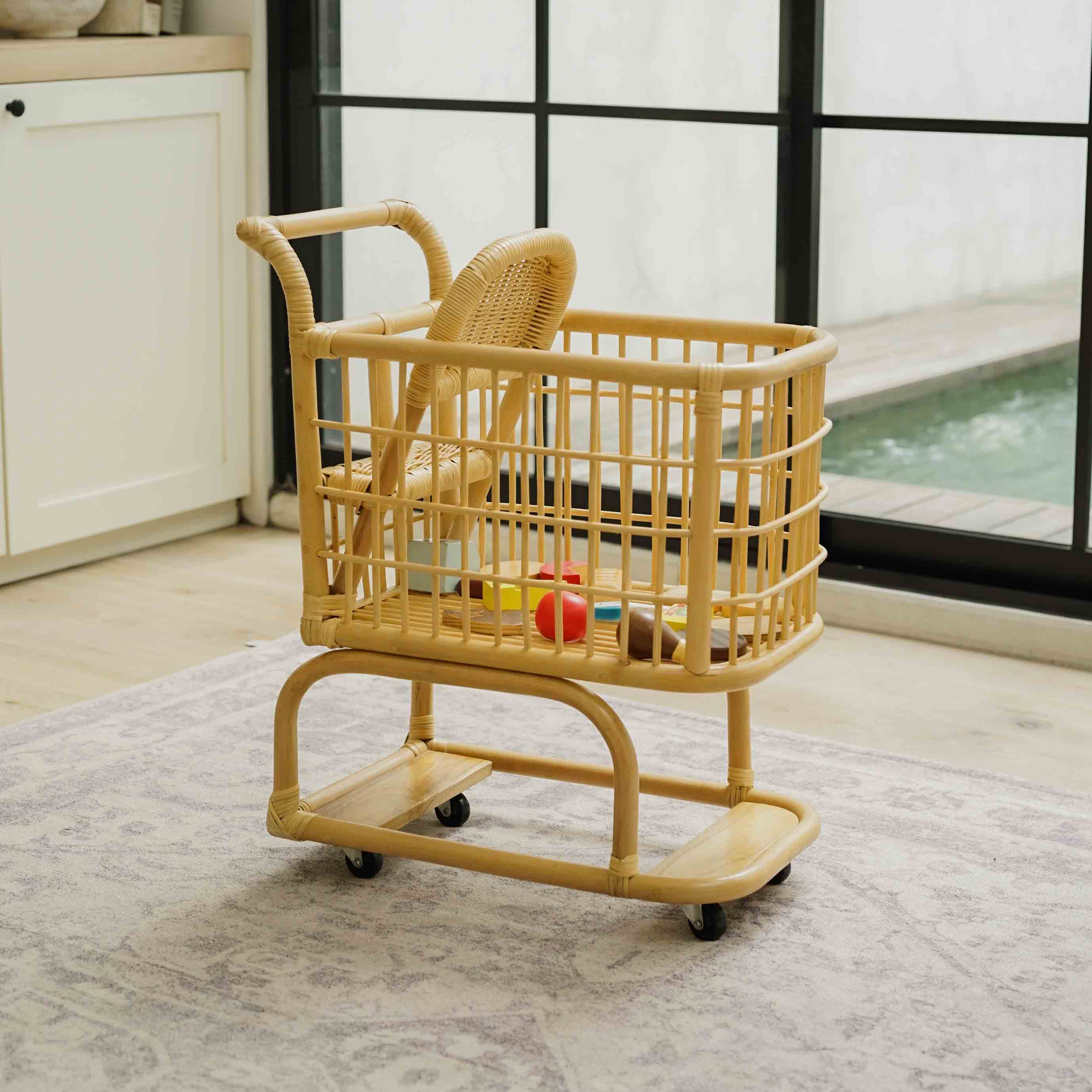 Side view of a handcrafted wicker rattan Kids Shopping Cart by MOMIJI featuring smooth rolling wheels and a spacious basket filled with grocery toys