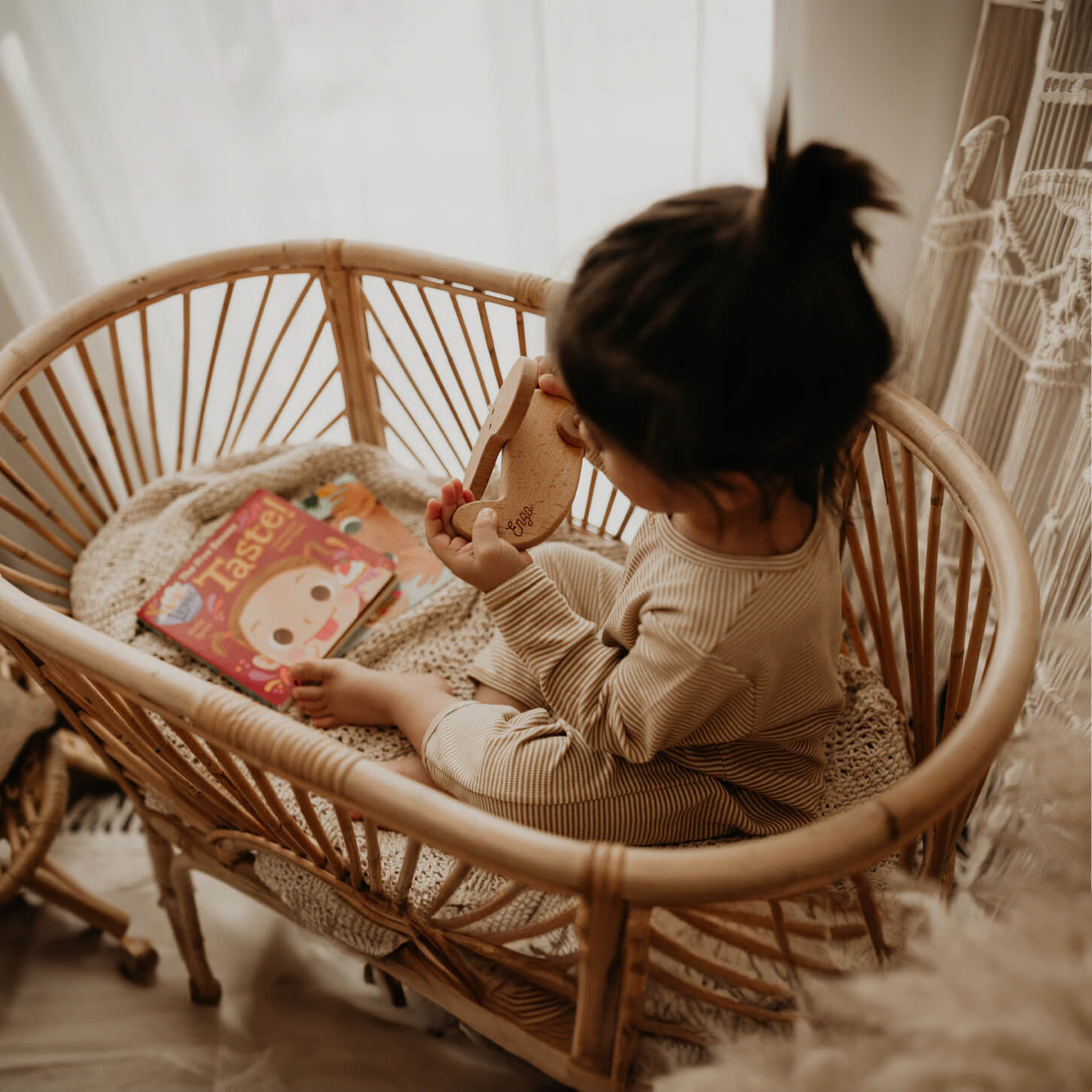 Top view of a child sitting and playing with toys inside the Kraton Bassinet by MOMIJI with children’s books nearby.