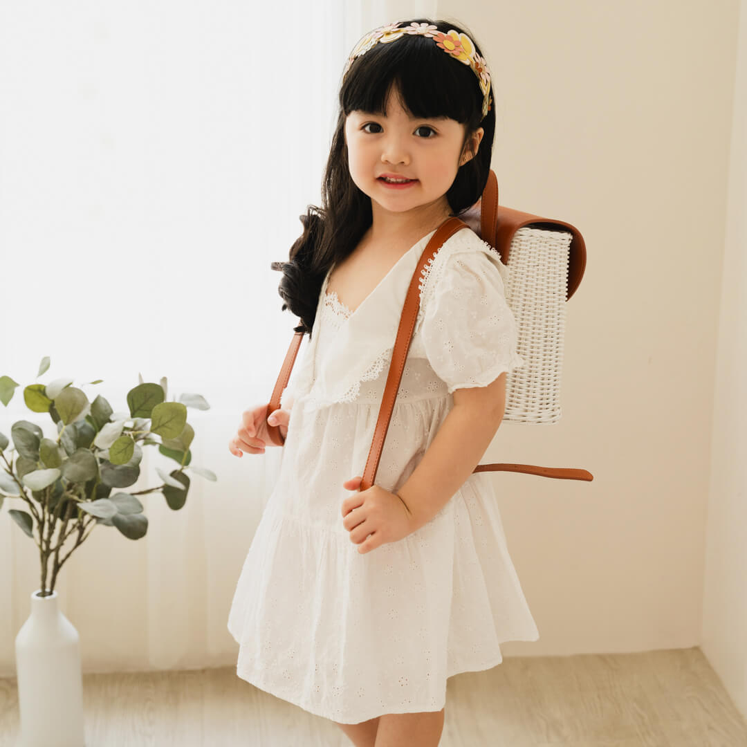 Happy child wearing the handcrafted rattan Layla Backpack by MOMIJI indoors.