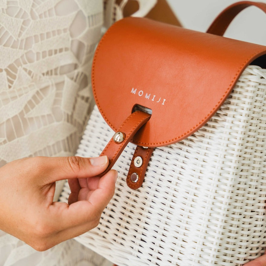 Close-up of a hand opening the leather lock on the handcrafted rattan Layla Backpack by MOMIJI.