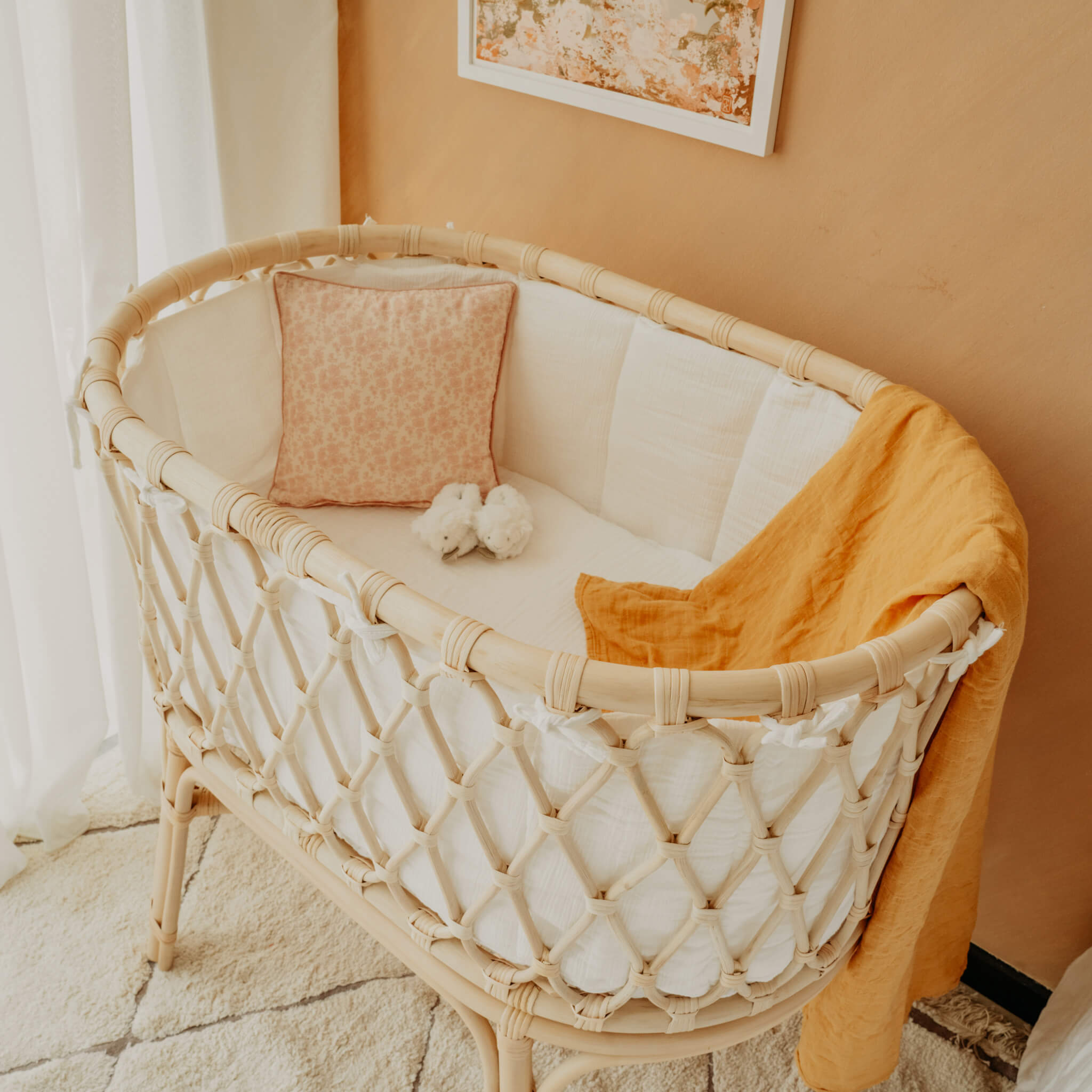 Layla Bassinet by MOMIJI styled with white bedding, an orange blanket, and pink in decorative room.