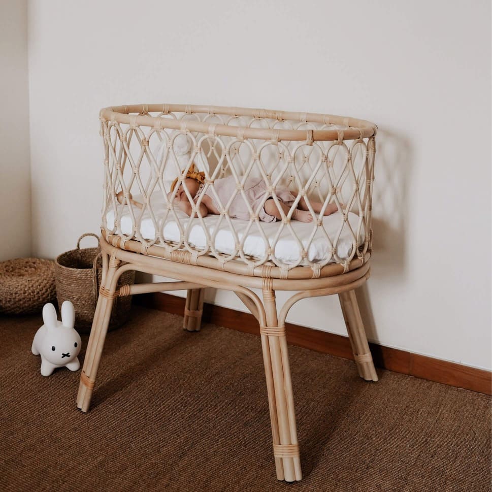 Layla Bassinet by MOMIJI with a baby inside, placed on a rug with baskets and toys nearby.