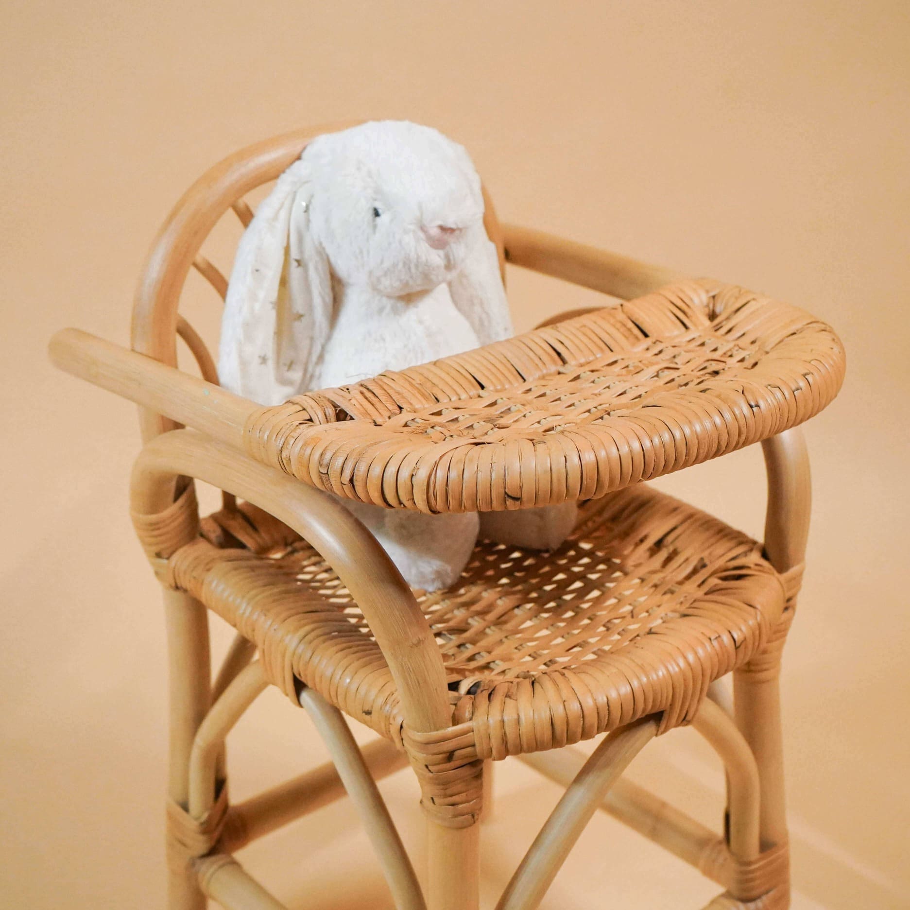 Close-up angled view of the handcrafted rattan wicker Layla Doll High Chair by MOMIJI with a bunny doll seated.