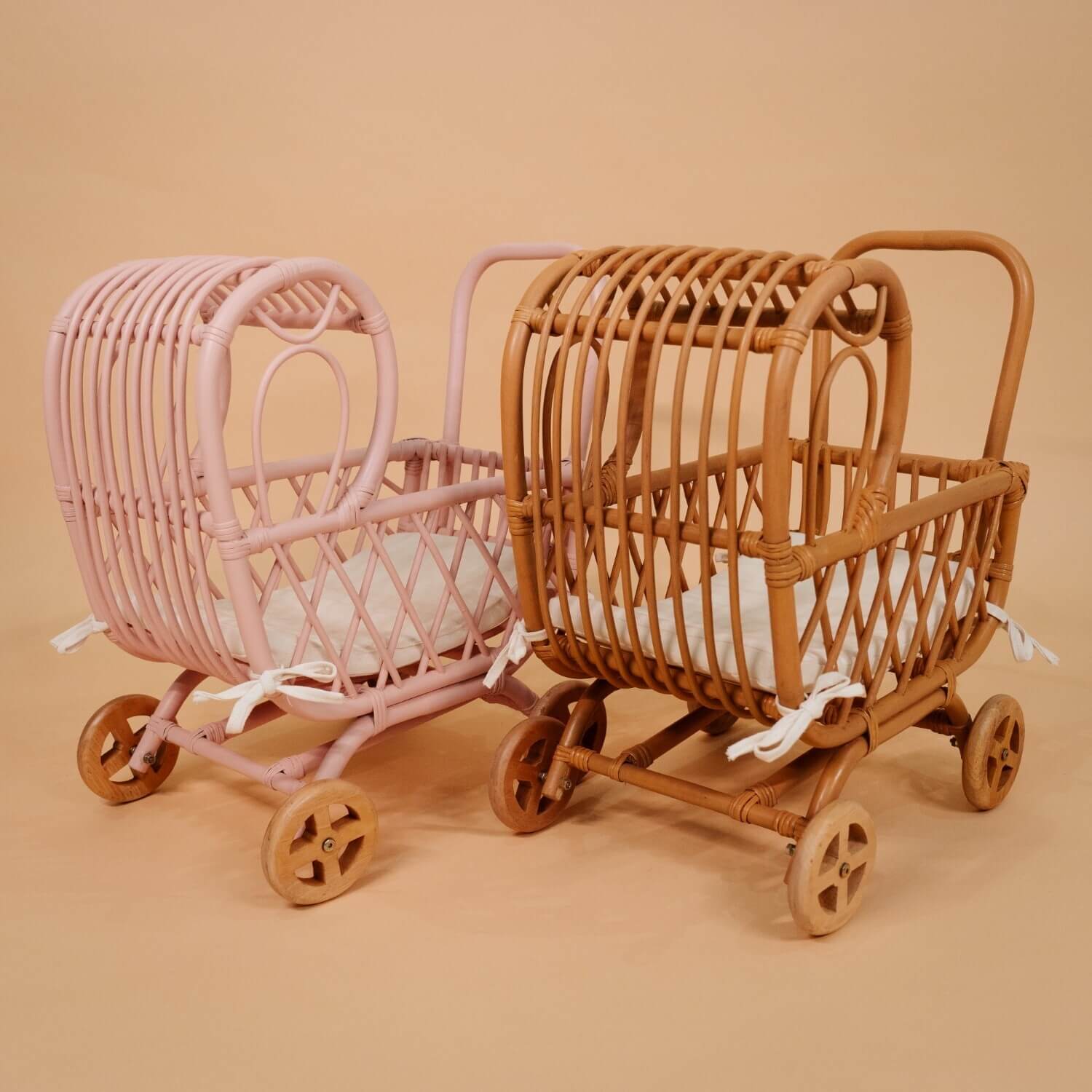 Rear view of the handwoven rattan Layla Toy Stroller by MOMIJI in pink and natural versions, with white seat pads inside.