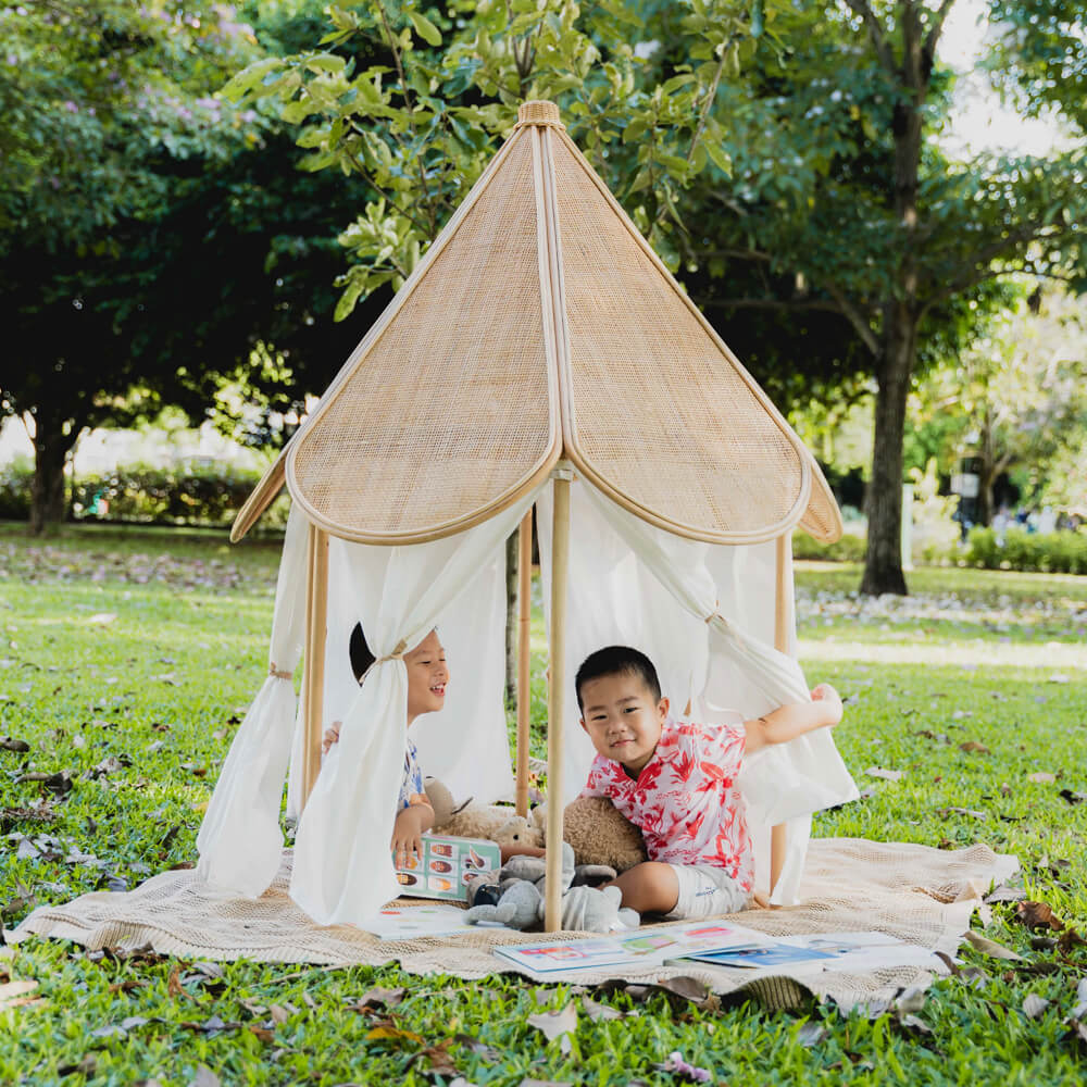 Two children sitting on a rug while playing under the Leon Circus Tent by MOMIJI in a garden.