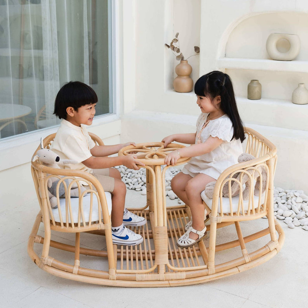 Two children smiling while playing on the Leon Rocking Bench by MOMIJI in a decorated indoor space.