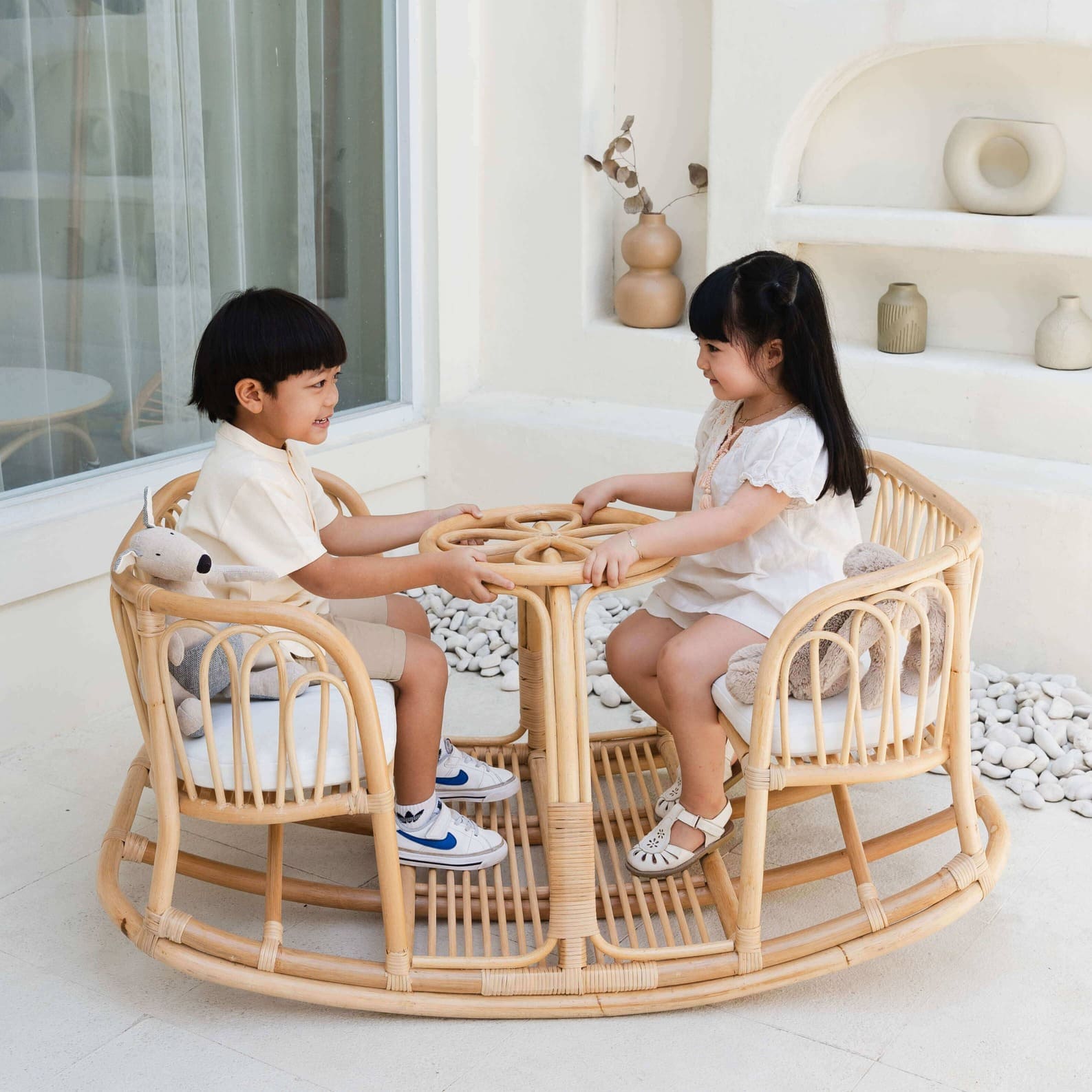 Two children smiling while playing on the Leon Rocking Bench by MOMIJI in a decorated indoor space.