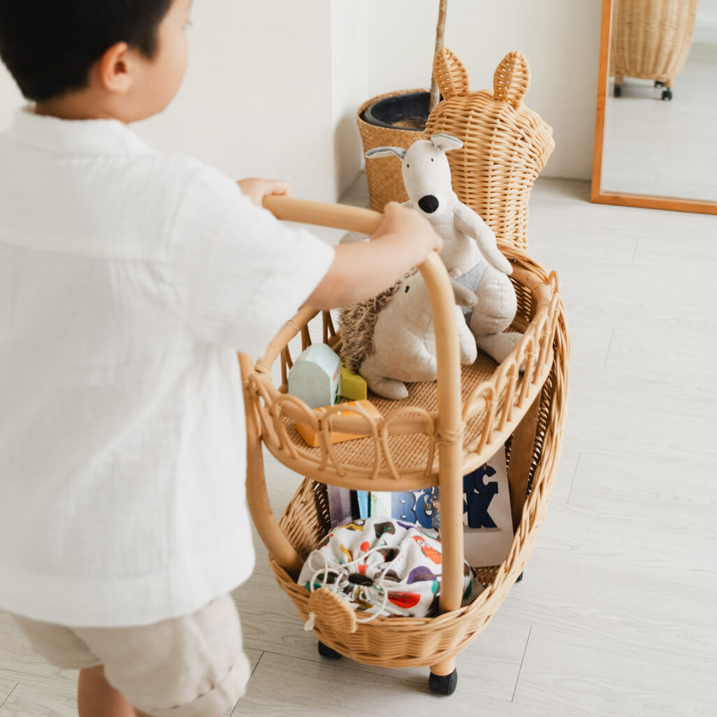 Back view of a child pushing a toy-filled Llama Craft Trolley by MOMIJI in a cozy room.