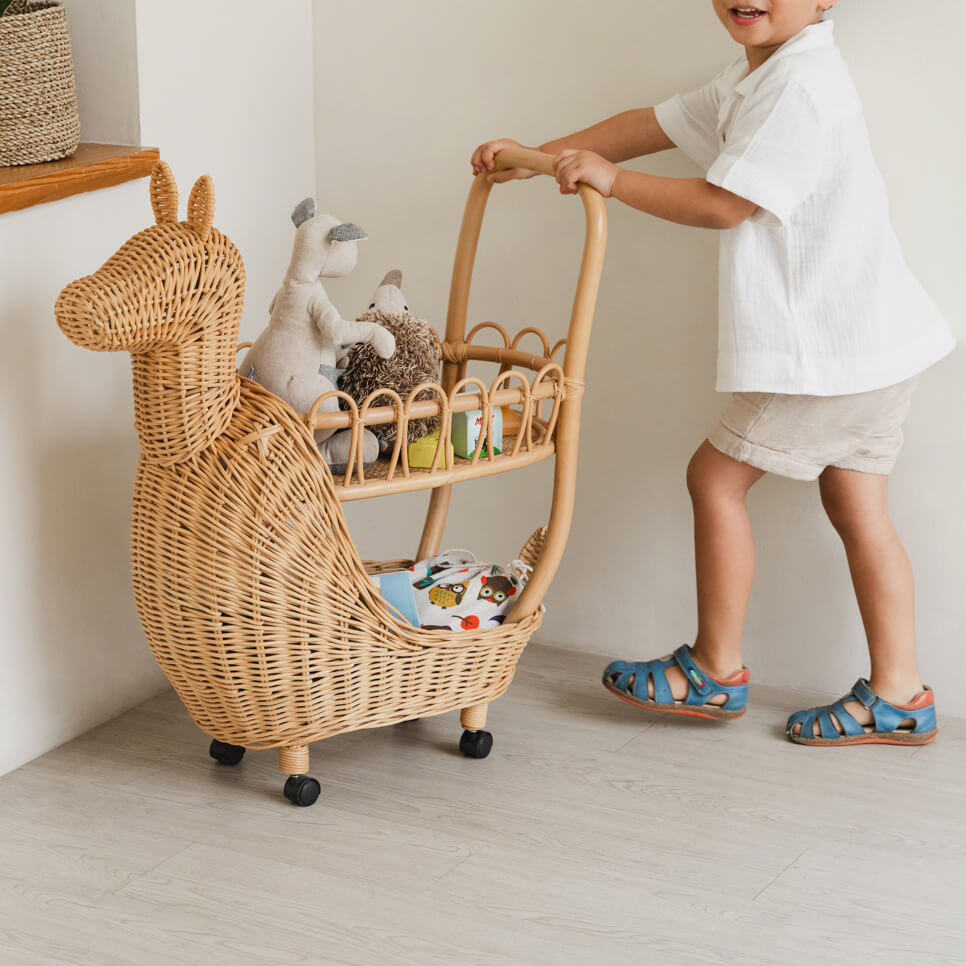 Smiling child pushing a Llama Craft Trolley by MOMIJI filled with toys in a bright indoor space.