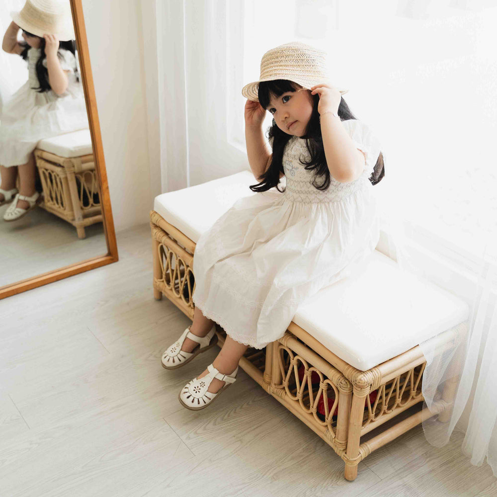 Child sitting on the Luke Kids Bench by MOMIJI holding a hat indoors.
